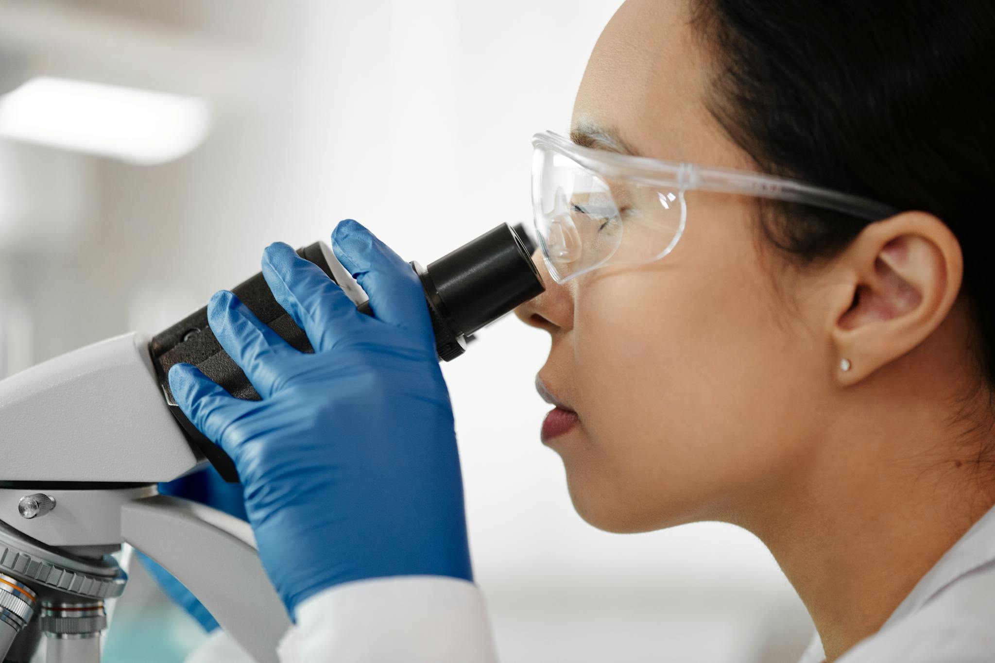 Scientist wearing safety glasses and gloves while examining samples with a microscope in the laboratory.