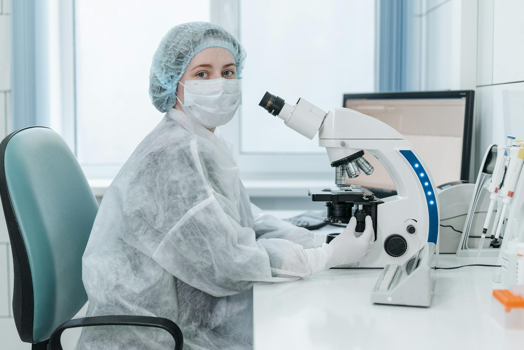 Woman lab technician examining samples with a trinocular microscope in a medical laboratory setting.